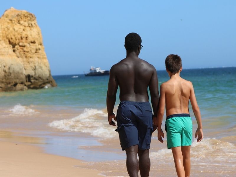 A photo of two boys, one black and one white, walking beside each other on a beach.