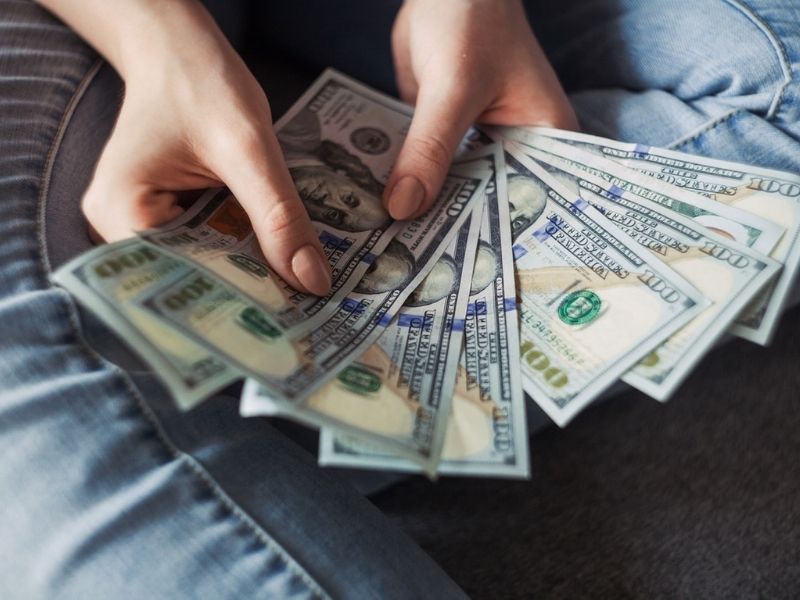 Photo of a woman holding ten 100-dollar bills to represent employee pay.