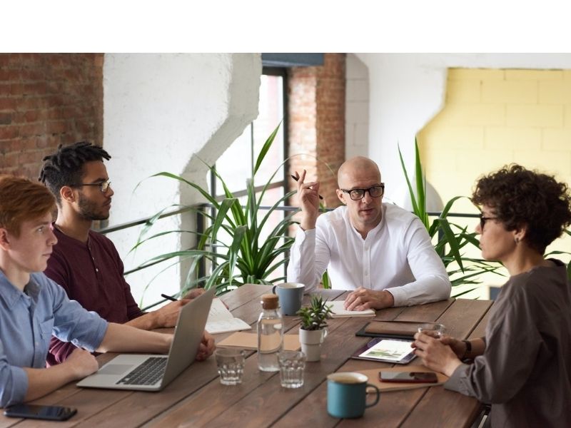 Four people around a table at a business meeting discussing how to have a successful discussion.