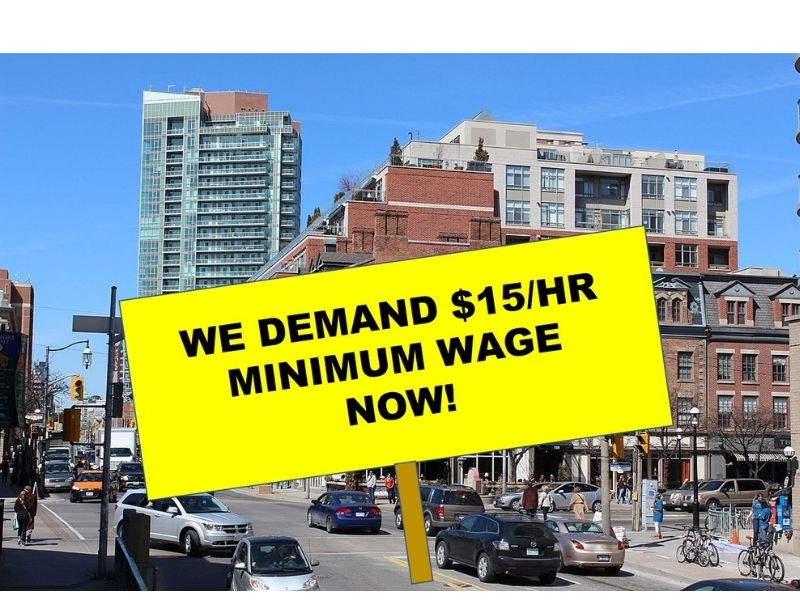 Sign that says We Demand $15/hr Minimum Wage Now! with a urban scene in the background.